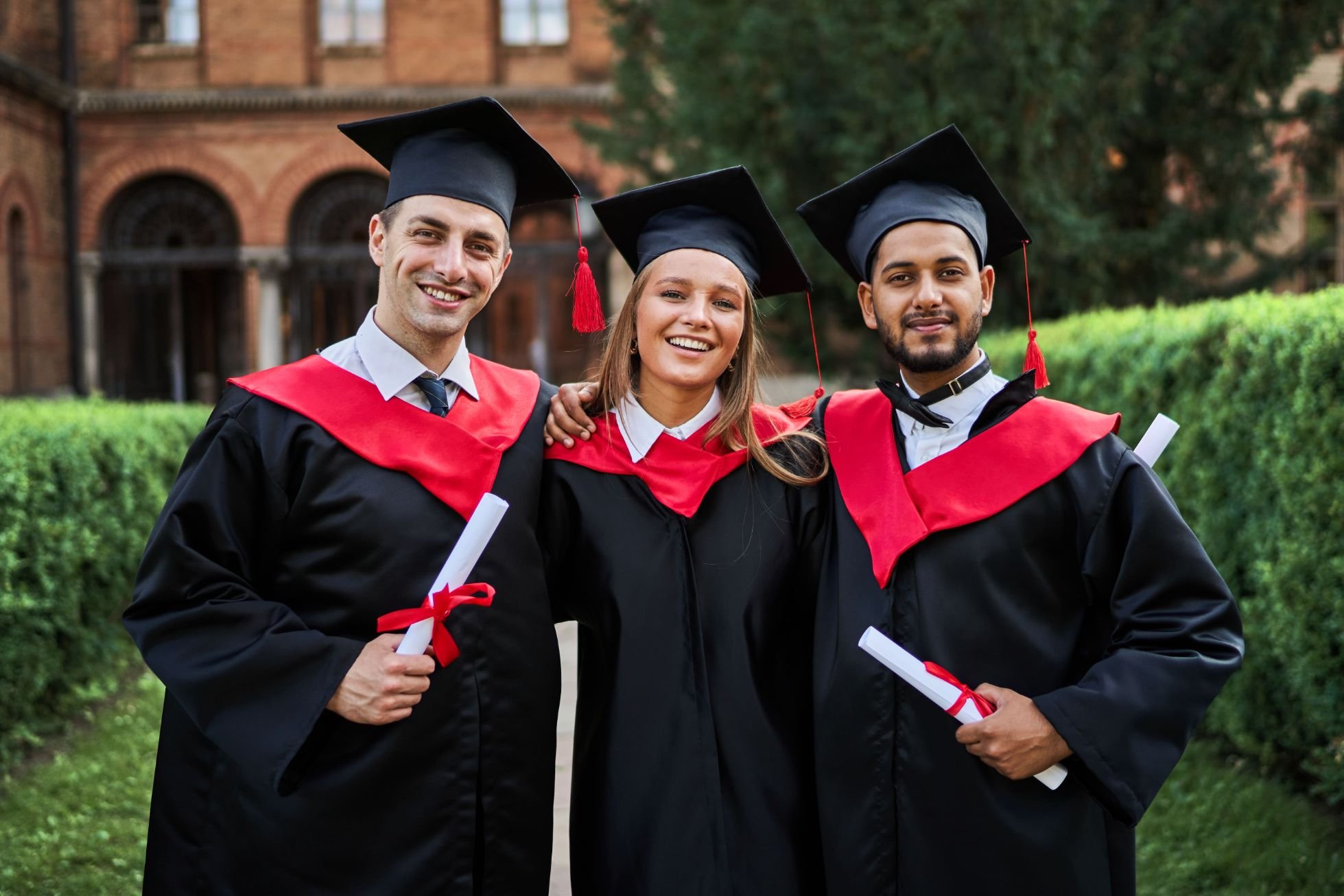 Portrait three smiling graduate friends graduation robes university campus with diploma(1)