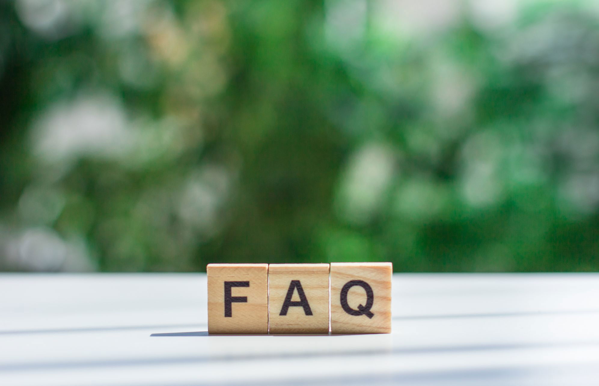 Word faq message sign wooden cubes light table against background green leaves soft focus frequently asked question concept